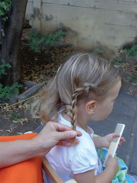Niña con una trenza, vista de espaldas mientras sostiene un peine.